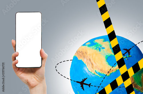 Prohibition of global transportation. Barrier tape on globe with a silhouettes of airplanes flying along the routes. Hand holding smartphone with mock up, copy space. The concept of air travel