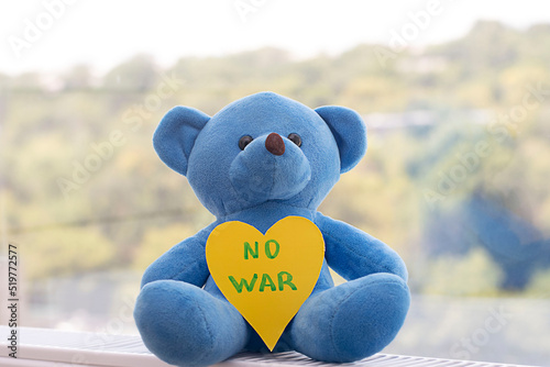 Concept. Children's soft toy, a blue teddy bear with the inscription no war on the background of the window.