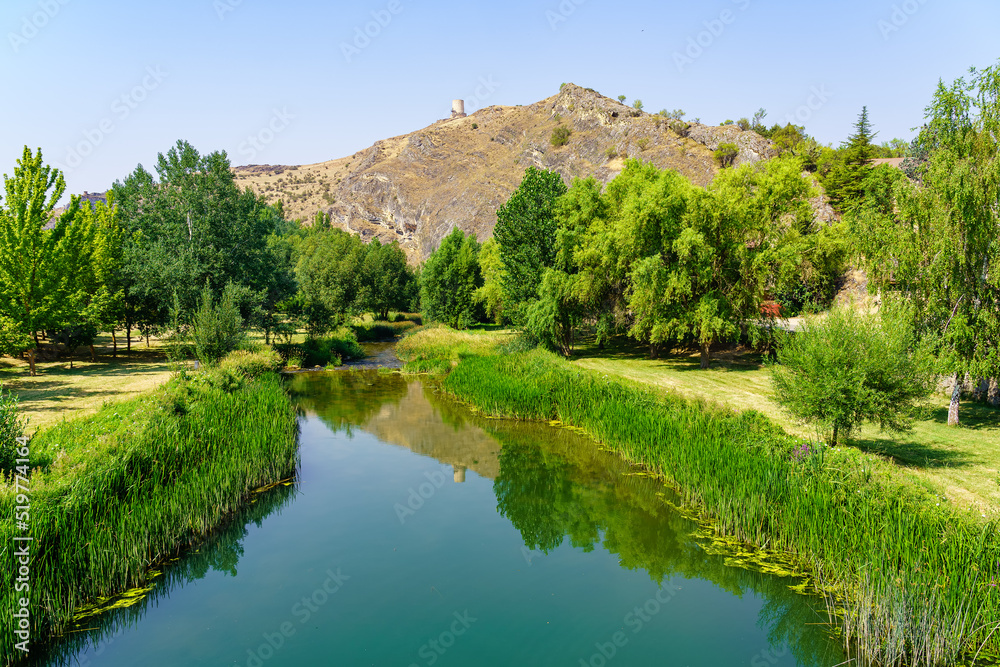 Hill with medieval tower at the top and stream of transparent waters passing calming next to the mountain, El Burgo de Osma.