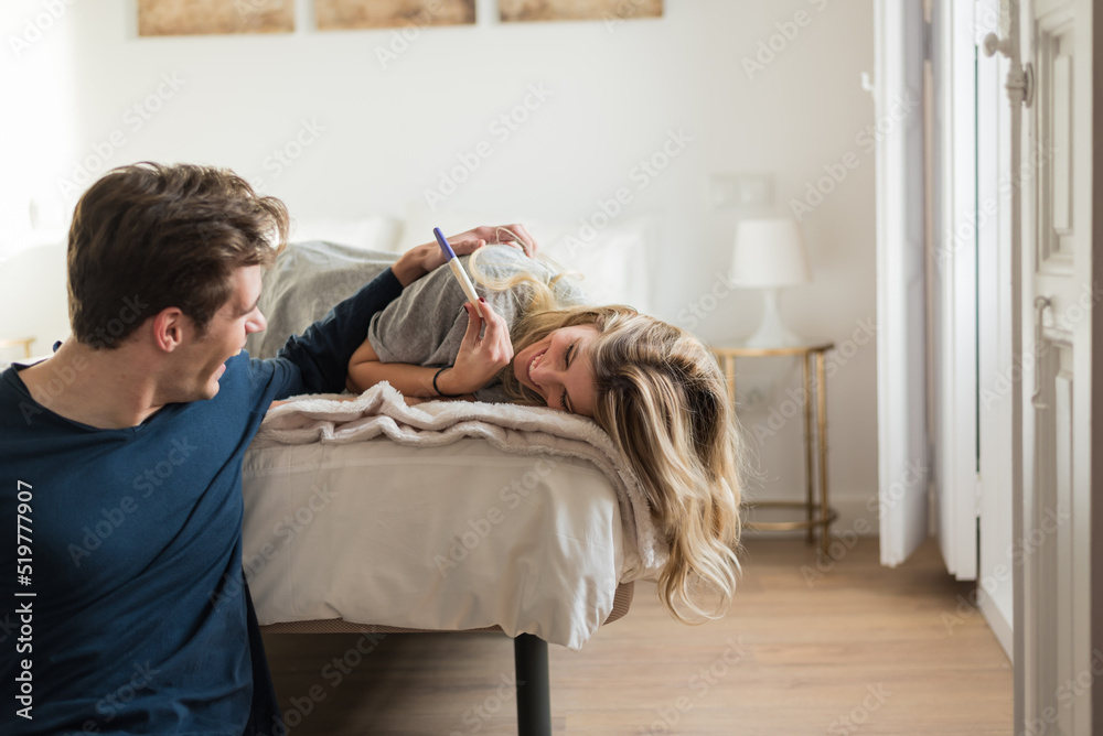 Happy couple looking at pregnancy test on bed - obrazy, fototapety, plakaty 