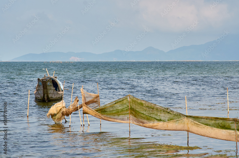 Obraz premium a fishing boat and nets are stretched on sticks against the backdrop of mountains on the horizon. Vietnamese fishing boat