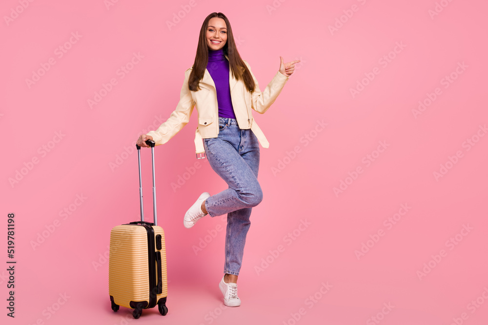 Full size photo of sweet young lady index promotion hold valise wear jacket jeans shoes isolated on pink color background