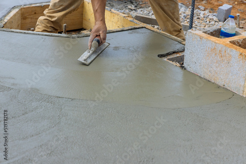 Mason worker holding steel trowel is being smoothed with plastering concrete to a cement floor in construction site