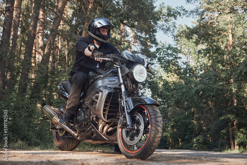 Young male biker in a helmet travels on a motorcycle alone, on a road in the forest