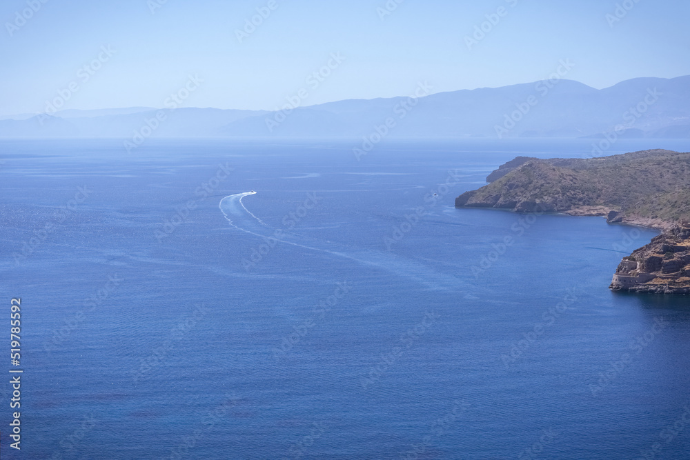Hypnotic sea horizon with small islet Spinalonga, mountain hills and speed boat's movement in  blue water. Plaka, Crete island, Greece. Travel vacation concept.