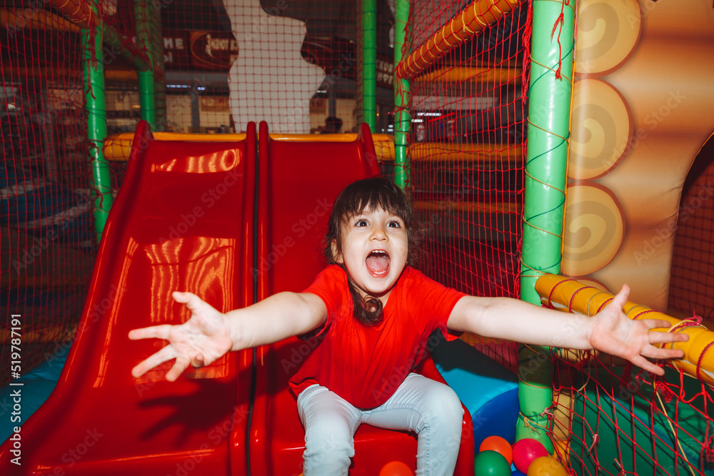 A happy little girl is having fun in an indoor play center. A child plays with colored balls in