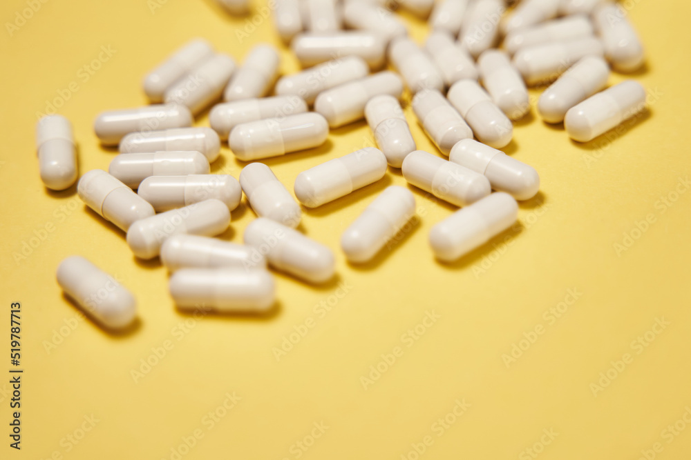scattered large white capsules like tablets. white pills are lying on a yellow background