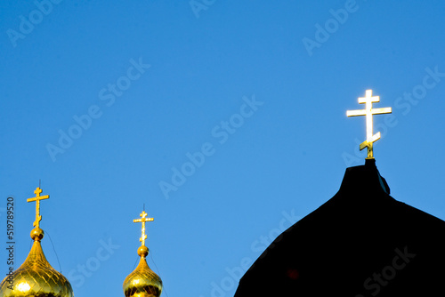 A golden Orthodox cross shines from sun against a blue sky. Christian photo with copy space