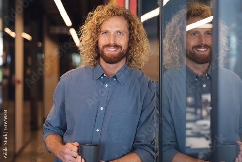 Portrait of smiling caucasian young businessman with coffee mug in creative office