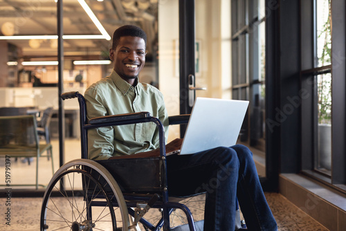 Fotografia Smiling african american businessman with disability using laptop in wheelchair