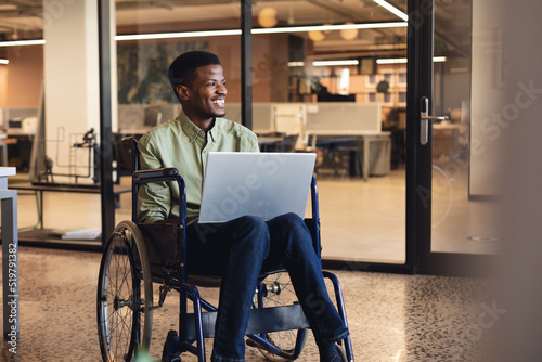 Fototapeta Smiling african american businessman with disability using laptop in wheelchair