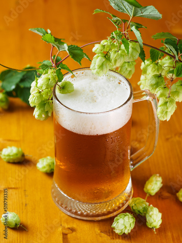 A mug of light beer on a wooden table, green cones of hops