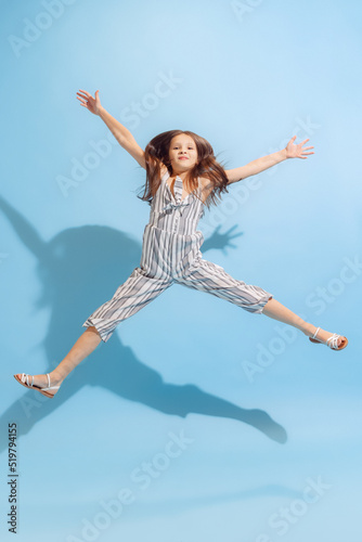 Happy school-age girl, kid in summer clothes posing isolated on light blue background. Concept of children emotions, fashion, beauty, school and ad