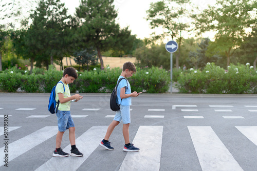 Two children look at their mobile phones while crossing a crosswalk on the street. Concept of mobile phone addiction