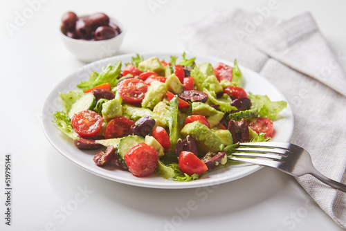 Salad with lettuce, cucumbers, tomatoes, olives and avocados in white plate on the table