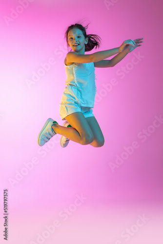 Happy little beautiful girl, school girl in casual outfit isolated on pink background in neon. Concept of children emotions, fashion, beauty, ad © master1305