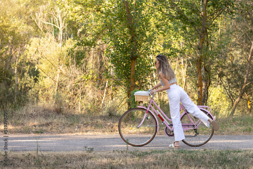 Side view of young elegant woman getting on retro pink bike in the middle of nature in spring time