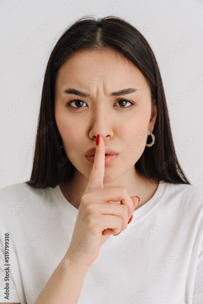 Asian displeased woman wearing t-shirt showing silence gesture Asian displeased woman wearing t-shirt showing silence gesture