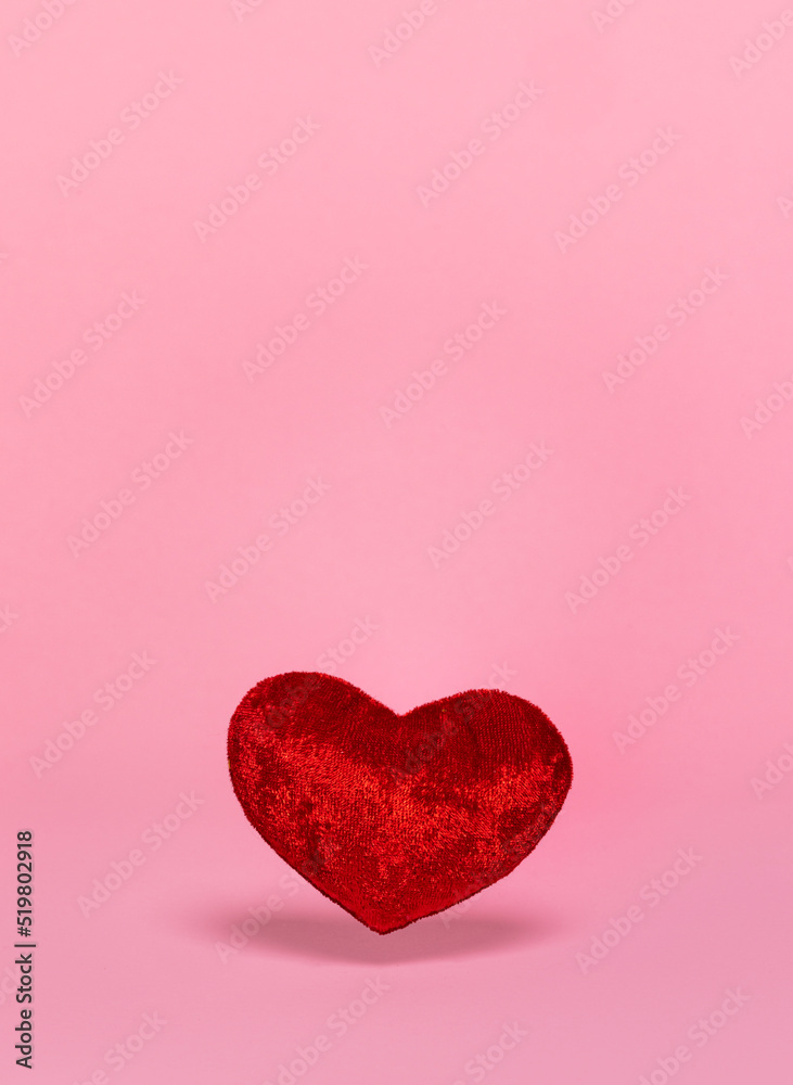 Red velvet fabric heart shaped toy, floating in air. Isolated on a soft pink background.