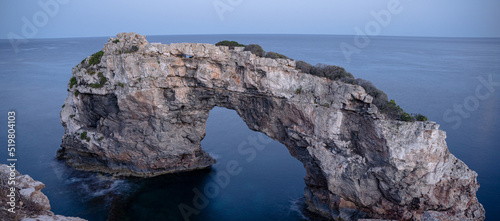The archway es pontas at Mallorca, Spain in the dawn with some bushes in the foreground. photo