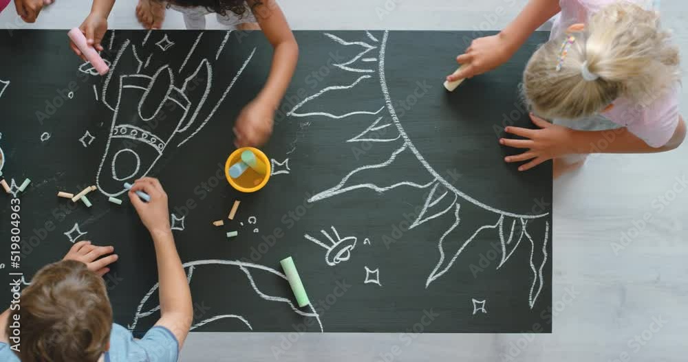 Creative, drawing and fun activity in a kids classroom with chalk and blackboard from above. Group of diverse children learning together and creating an interactive, educational art project in class