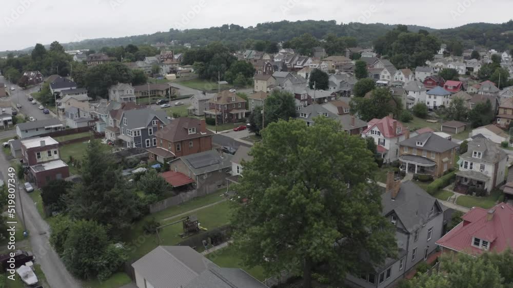 An orbiting aerial establishing shot of a typical Pennsylvania middle-class residential neighborood on an overcast summer day. Pittsburgh suburbs.  	