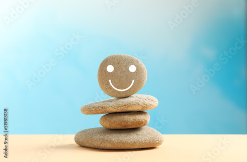 Stack of stones with drawn happy face on beige table against light blue background. Zen concept