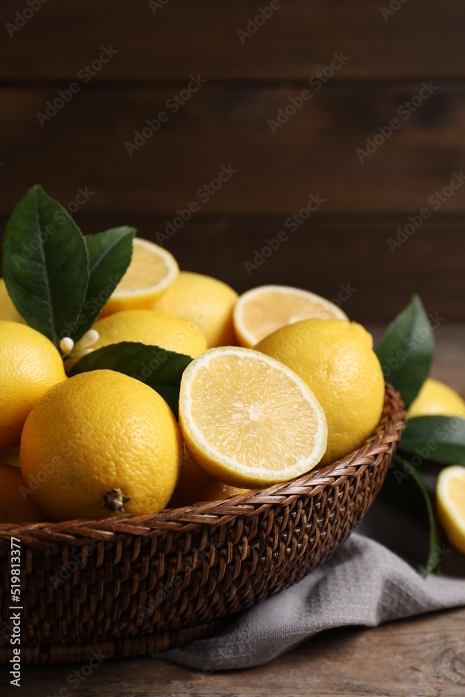 Many fresh ripe lemons with green leaves on wooden table