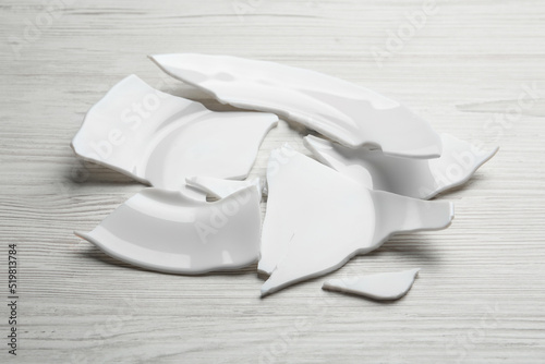 Pieces of broken ceramic plate on white wooden table