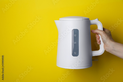 Woman holding modern electric kettle on yellow background, closeup. Space for text photo
