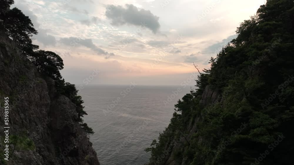 Slow move between rugged coastal cliffs to morning sunrise on calm sea Slow move between rugged coastal cliffs to morning sunrise on calm sea
