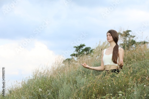 Teenage girl meditating on hill. Space for text