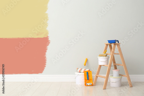 Decorator's kit of tools and paints near white wall with samples of different paints indoors