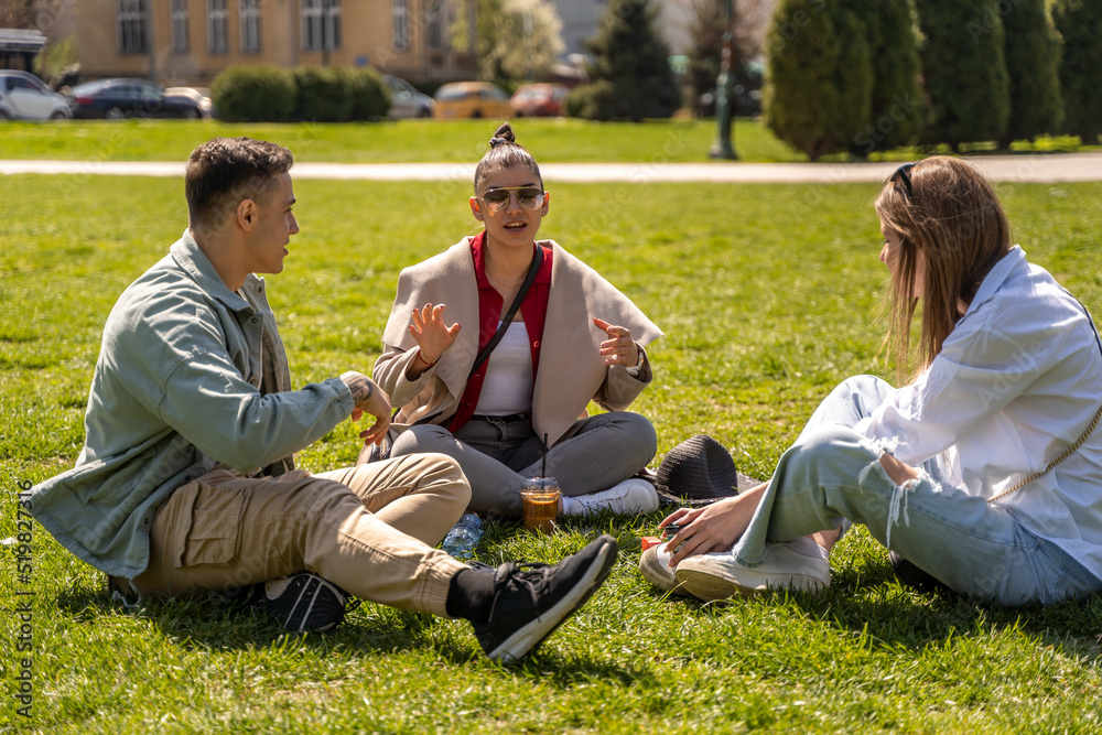 Group of cheerful friends spending time together while sitting on green lawn Group of cheerful friends spending time together while sitting on green lawn