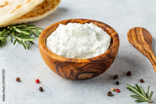 Homemade greek tzatziki sauce in an olibe wood bowl bowl on a light stone background. Close-up, horizontal image, copy space