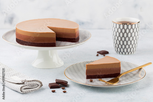 Triple chocolate mousse cake on a cake stand on white background