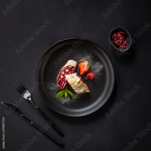 freshly baked cherry strudel on a black plate on a dark background, classic recipe, view from above, flat lay