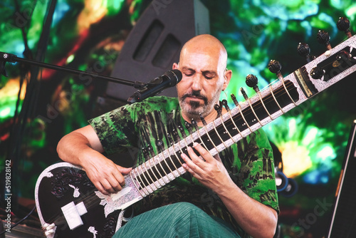 A male sitar player playing onstage at a summer festival