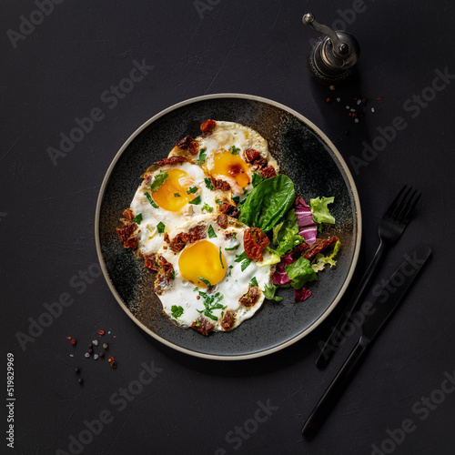 Fried egg. fried egg on a plate. Salted and spiced fried egg with fresh salad leaves, black background.