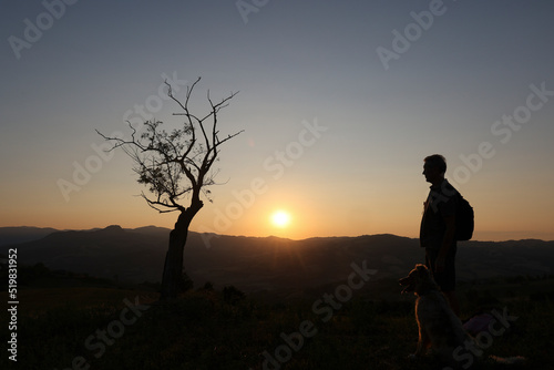 silhouette of man and his dog looking sunset from the top of the hill