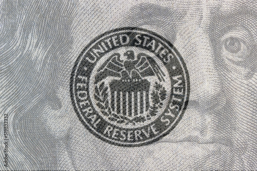 Federal Reserve System seal overlay on a hundred dollar bill. The Fed's responsibilities include setting interest rates and regulating financial markets.