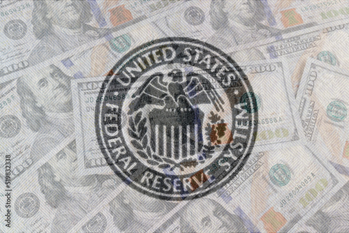Federal Reserve System seal overlay on a bed of hundred dollar bills. The Fed's responsibilities include setting interest rates and regulating financial markets.