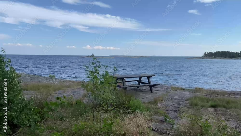 Empty wooden picnic table and bench on cliffs outdoors in the Swedish archipelago, surrounded by coastal nature and landscape with the sea in the background on this windy day. Footage made in Sweden. Empty wooden picnic table and bench on cliffs outdoors in the Swedish archipelago, surrounded by coastal nature and landscape with the sea in the background on this windy day. Footage made in Sweden.