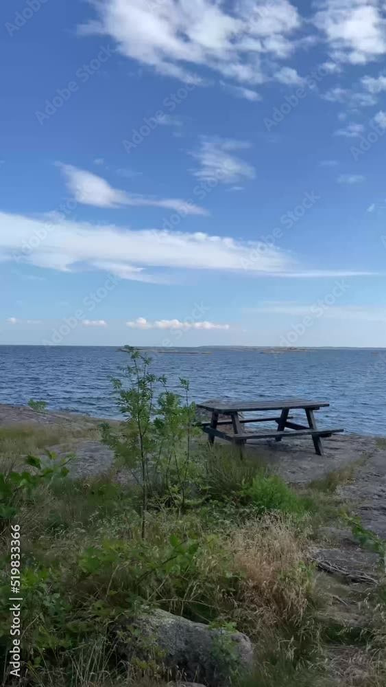 Vertical video of scenic view with empty wooden picnic table and bench on cliffs outdoors in the Swedish archipelago, surrounded by the sea, coastal nature and landscape. Footage made in Sweden. Vertical video of scenic view with empty wooden picnic table and bench on cliffs outdoors in the Swedish archipelago, surrounded by the sea, coastal nature and landscape. Footage made in Sweden.