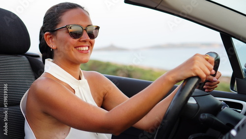 Woman alone in a black convertible car looks at the sunset in front of the sea and is moved by how wonderful it is, she feels free and happy during her vacation alone, independent and strong woman