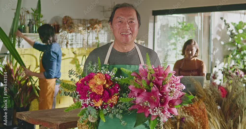 Asian American business entrepreneur owner of flower shop standing holding two bouquet of flower arrangements smiling at camera. Small business concept of floriculture store with employee working in t Asian American business entrepreneur owner of flower shop standing holding two bouquet of flower arrangements smiling at camera. Small business concept of floriculture store with employee working in t