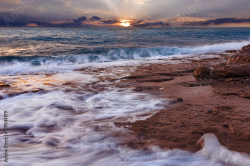 Beautiful colorful sunset over the sea with waves and rocky coastline. Peaceful Landscape with setting sun over the horizon