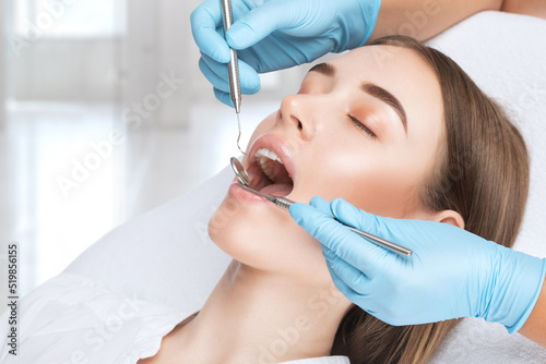 A dentist doctor treats caries on a tooth of a young beautiful woman in a dental clinic. Tooth filling. photo