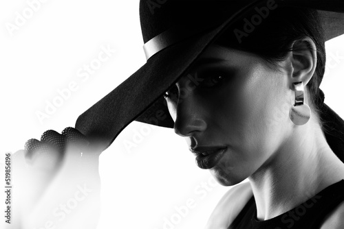 Elegant woman in a black dress and black hat on a white background.