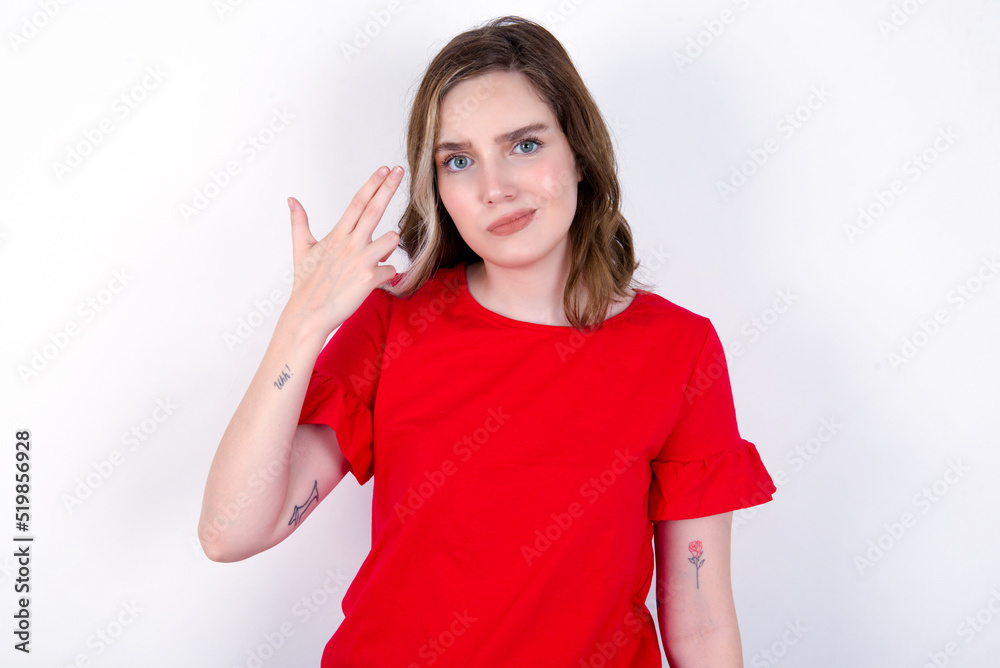 Unhappy young caucasian woman wearing red T-shirt over white background makes suicide gesture and imitates gun with hand, curves lips, keeps two fingers on temple Unhappy young caucasian woman wearing red T-shirt over white background makes suicide gesture and imitates gun with hand, curves lips, keeps two fingers on temple